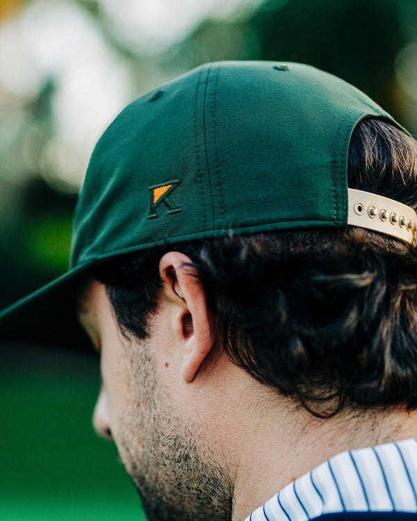 Person wearing a green cap with a logo, looking away from the camera.