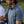 A man wearing a blue and white striped polo shirt with short sleeves, standing on a golf course.